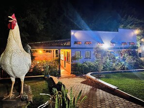 A large white rooster statue in a garden area with a building featuring multiple windows and a well-lit entrance. - Nkokonjeru White Cove Mbarara (Mbarara)