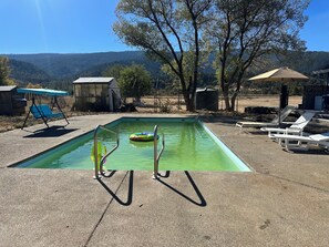 Ein rechteckiger Pool mit Metallleiter, umgeben von Liegestühlen und einer kleinen Gartenhütte.