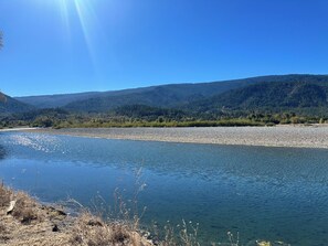 Ein Fluss mit steiniger Uferböschung und einem bewaldeten Berg im Hintergrund.