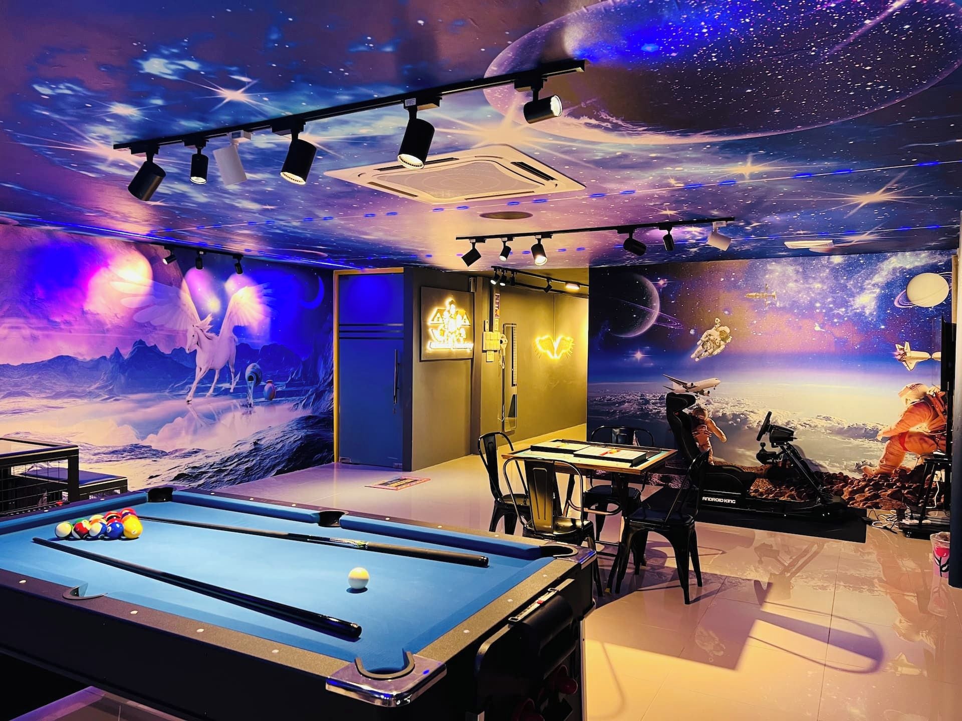A room with a pool table, a billiards table, and a space-themed mural.