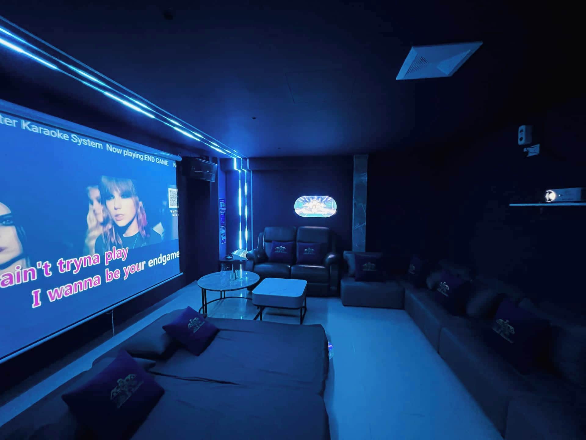 A modern home theater room with a large screen, comfortable seating, and a sound system.