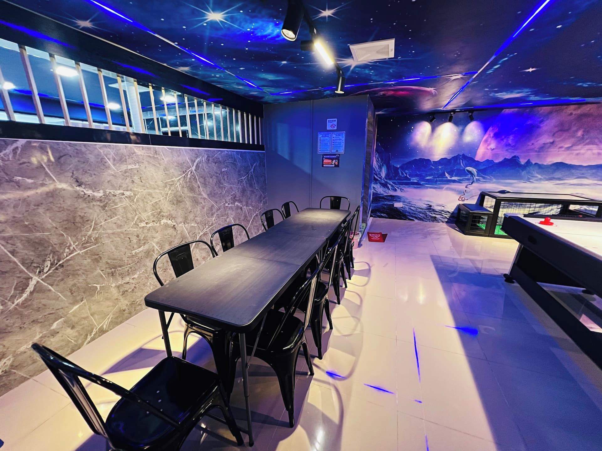 A conference room with a long table and chairs, a marble wall, and a mural of a celestial scene.