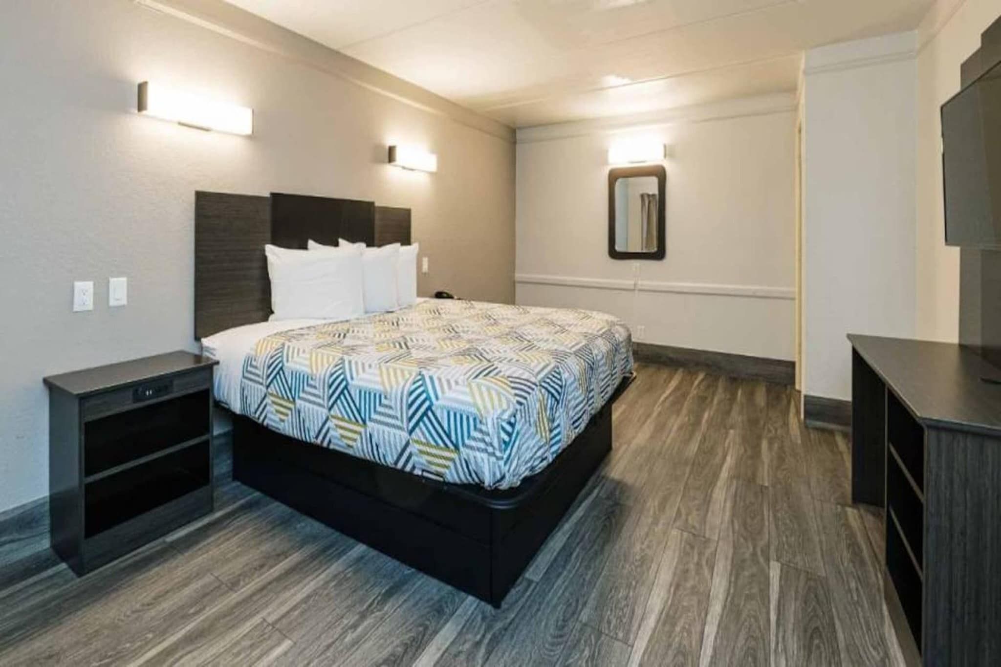 A hotel room with a bed, bedside tables, a mirror, and a TV stand.