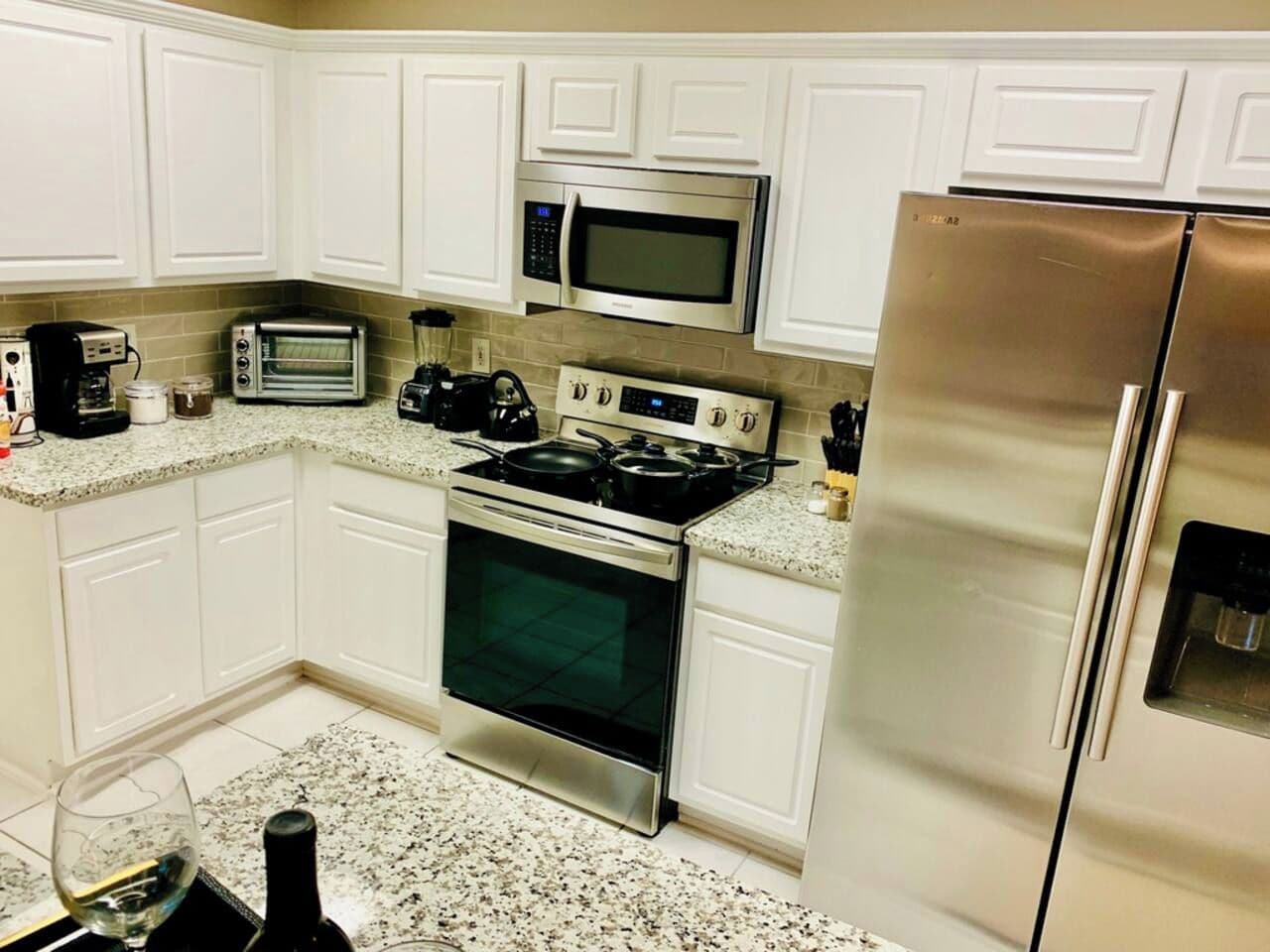A kitchen with white cabinets, stainless steel appliances including a microwave, oven, and refrigerator, and a granite countertop.