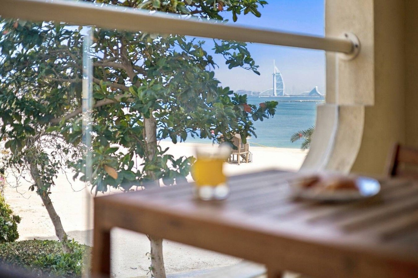 Une vue depuis une fenêtre donnant sur une plage, avec un palmier et, au loin, un pont.