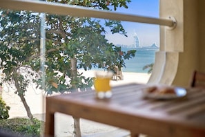 A view from a window overlooking a beach with a palm tree and a distant view of a bridge. - FIRST CLASS | 1BR | Tropical Escape On The Palm (Palm Jumeirah)