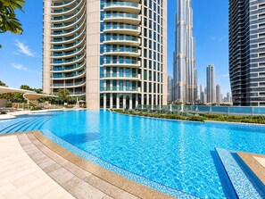 Una piscina amb vora corba, envoltada d'edificis moderns amb balcons.