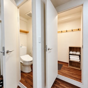 A bathroom with a toilet, a wooden floor, and a towel rack with folded towels. - Sanmi Tsutenkaku (Osaka)