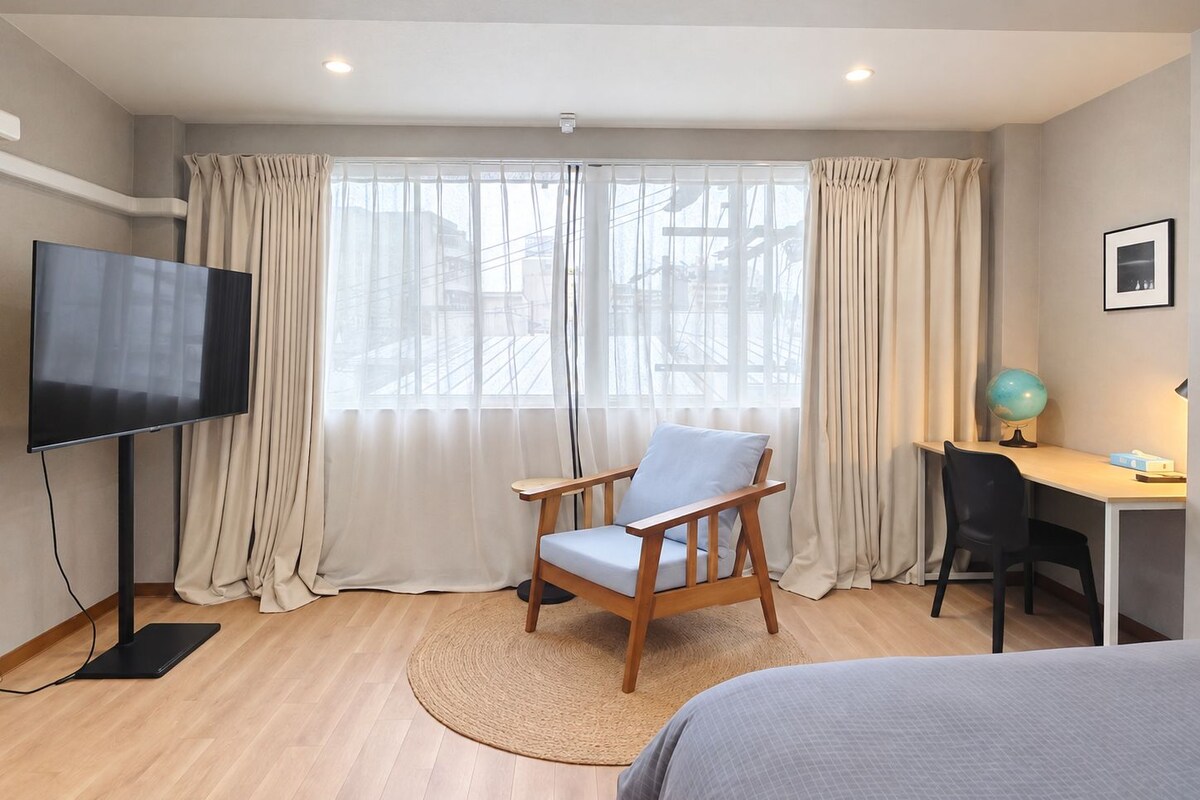 A hotel room with a bed, a desk with a chair, a television, and a window with curtains.