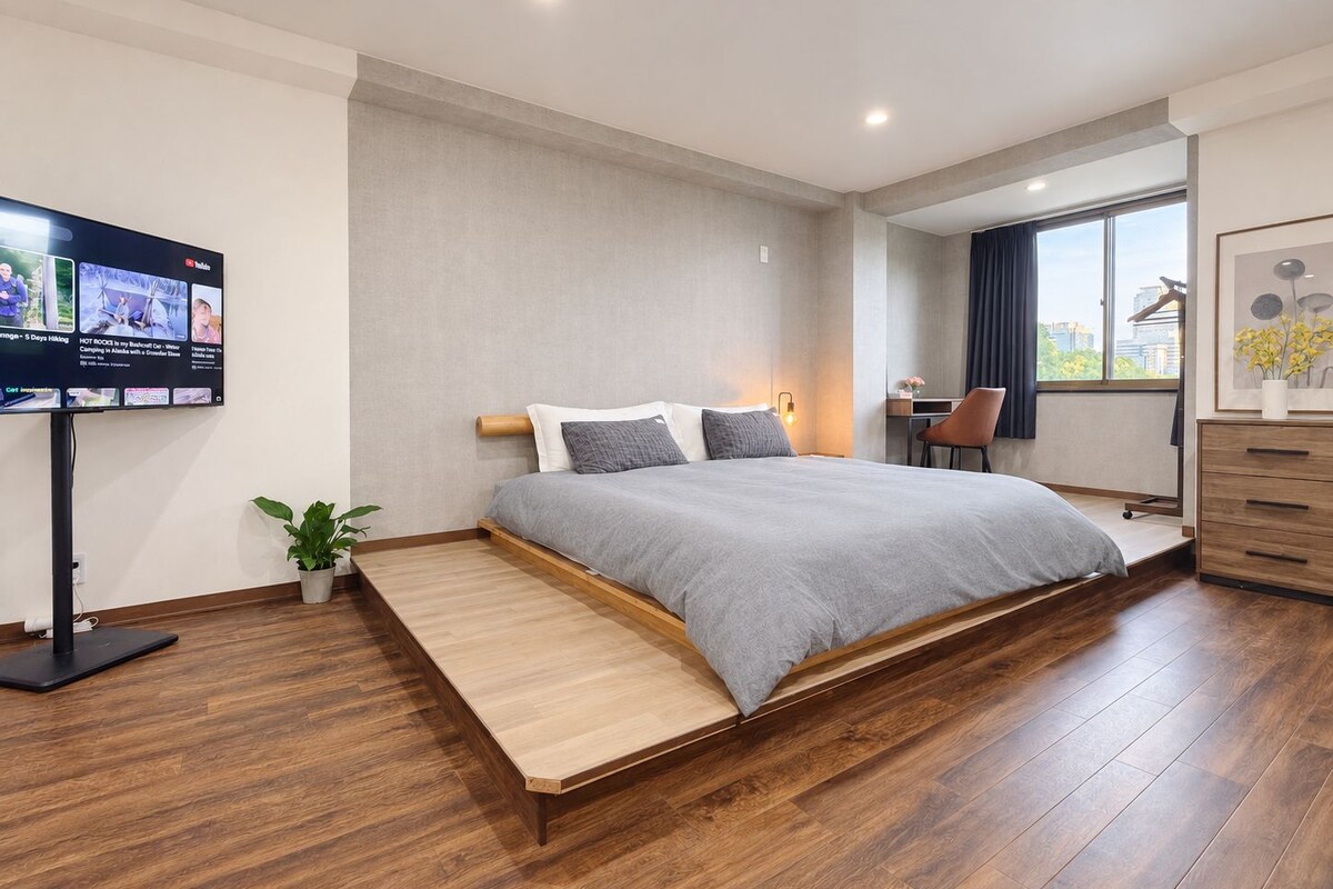 A modern bedroom with a bed, a desk, a chair, and a TV mounted on the wall.