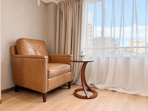 A tan leather armchair with a wooden base, positioned next to a round wooden table with a small potted plant. - Sanmi Tsutenkaku (Osaka)