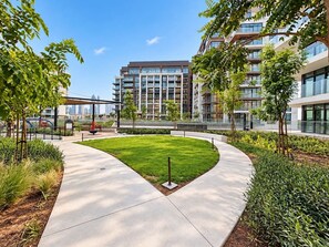 A landscaped courtyard with a central lawn, surrounded by modern buildings with large windows. - FIRST CLASS | 1BR | Elegant Escape At City Walk (City Walk)