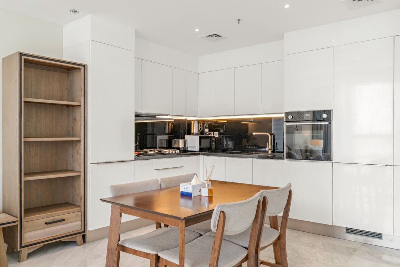 Una cocina moderna con armarios blancos, una mesa de comedor de madera y una estantería empotrada.
