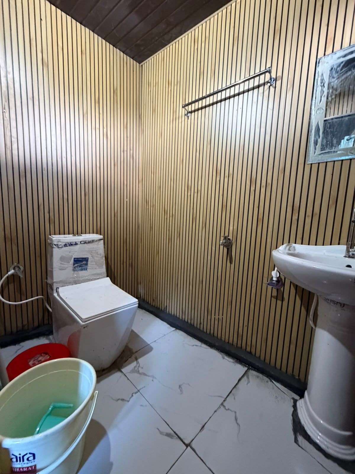 A small bathroom with a toilet, a sink, and a bucket.