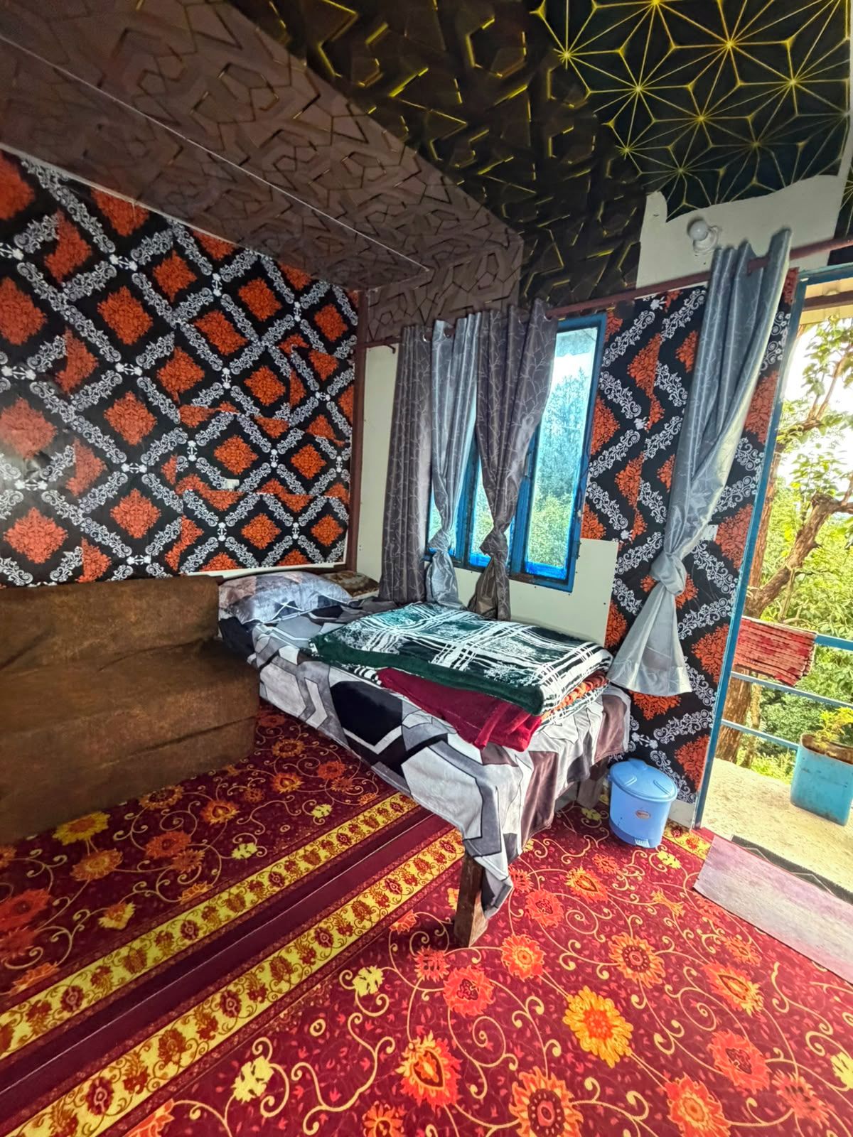 A room with a bed, a window with curtains, a patterned wall, and a red carpet.