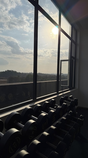 A gym with a row of dumbbells and a large window overlooking a landscape. - Modern 1 bedroom Westlands Nairobi (Nairobi)