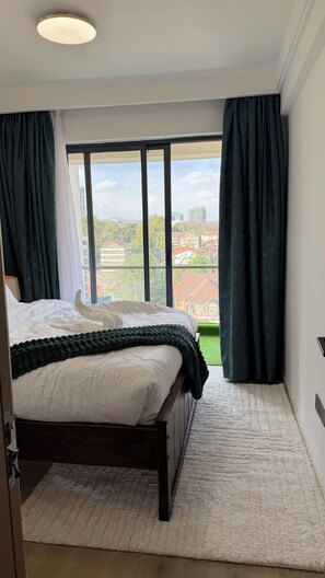 A bedroom with a large window, a bed, and a view of buildings. - Modern 1 bedroom Westlands Nairobi (Nairobi)