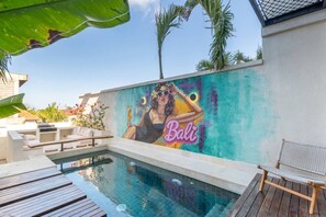 Ein Poolbereich mit Wandgemälde, Liegestühlen und einer Holzterrasse.