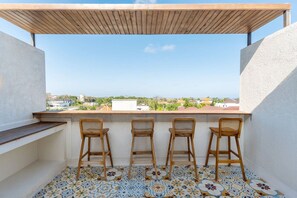 Ein Balkon mit einer Holz-Pergola, drei Korbstühlen und gemusterten Bodenfliesen.