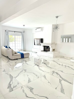 A spacious living room with a marble floor, a sofa with blue cushions, a fireplace, and a mounted TV. - Modern Luxury Home with Pool in Kiti - 4 bed 3 bath 2 kitchen (Kiti)