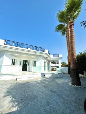 A modern white building with a balcony, a palm tree, and a sun design on the ground. - Modern Luxury Home with Pool in Kiti - 4 bed 3 bath 2 kitchen (Kiti)