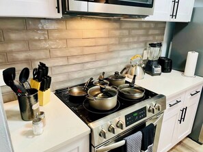 Een moderne keuken met een fornuis, pannen, een koffiezetapparaat en een broodrooster.