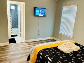 A bedroom with a bed, a television mounted on the wall, a window with blinds, and a wooden floor. - House 3-Bed 2-Bath FREE Parking (The Woodlands)