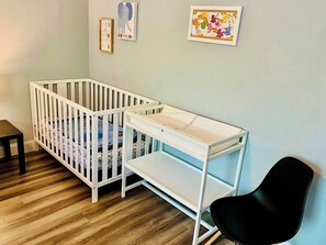 A room with a white crib, a black chair, and a white shelf unit. - House 3-Bed 2-Bath FREE Parking (The Woodlands)