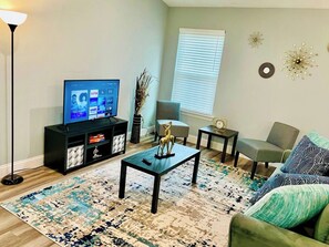 A living room with a flat-screen TV, a coffee table, a sofa, a side table, and a floor lamp. - House 3-Bed 2-Bath FREE Parking (The Woodlands)