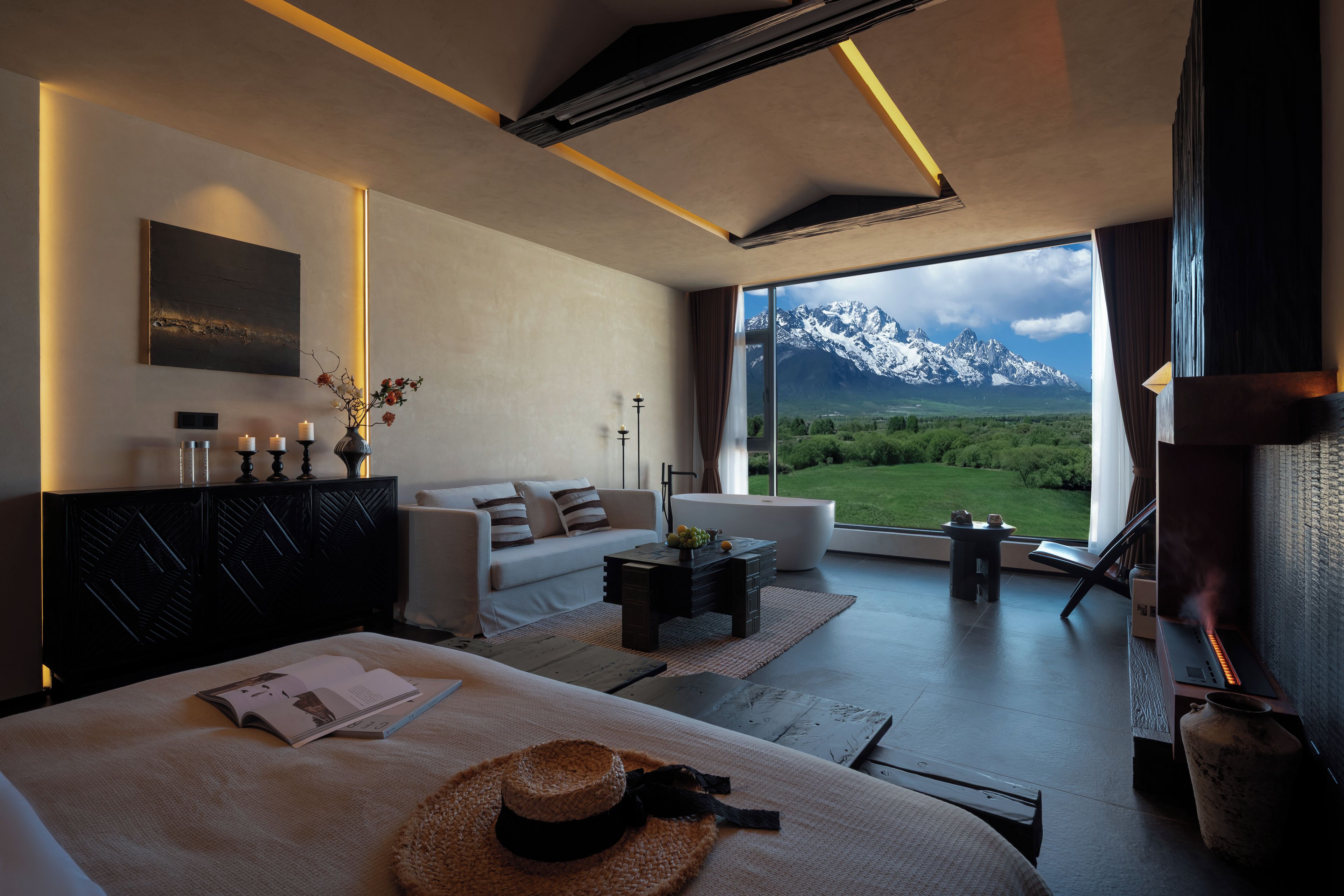 Une chambre d’hôtel moderne dotée d’une grande fenêtre donnant sur les montagnes, d’un coin salon confortable et d’une cheminée.