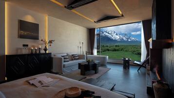 Habitación de hotel moderna con un amplio ventanal que ofrece vistas a la montaña, un rincón de descanso acogedor y una chimenea.
