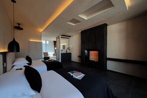 A modern hotel room with a large bed, a bedside table, a flat-screen TV, and a fireplace.