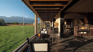 A covered outdoor seating area with a view of a grassy field and mountains.
