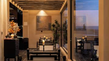 A hotel lobby with a wooden ceiling, a large painting on the wall, and a view of the ocean through the windows.