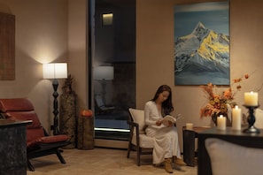 A cozy reading area with a chair, a table with candles, and a painting of a mountain.
