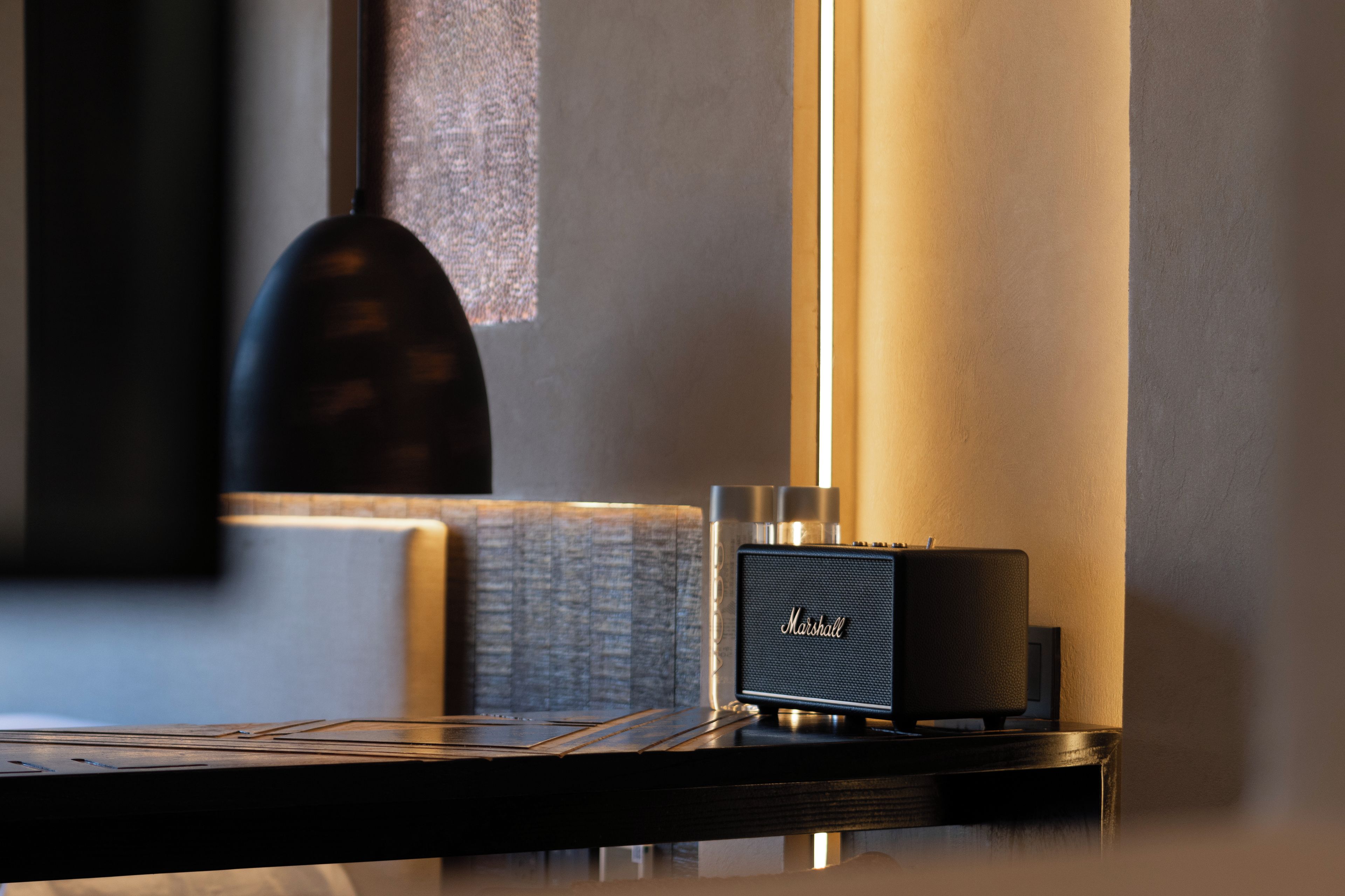 Un escritorio moderno con una computadora portátil, un altavoz Marshall y una lámpara.