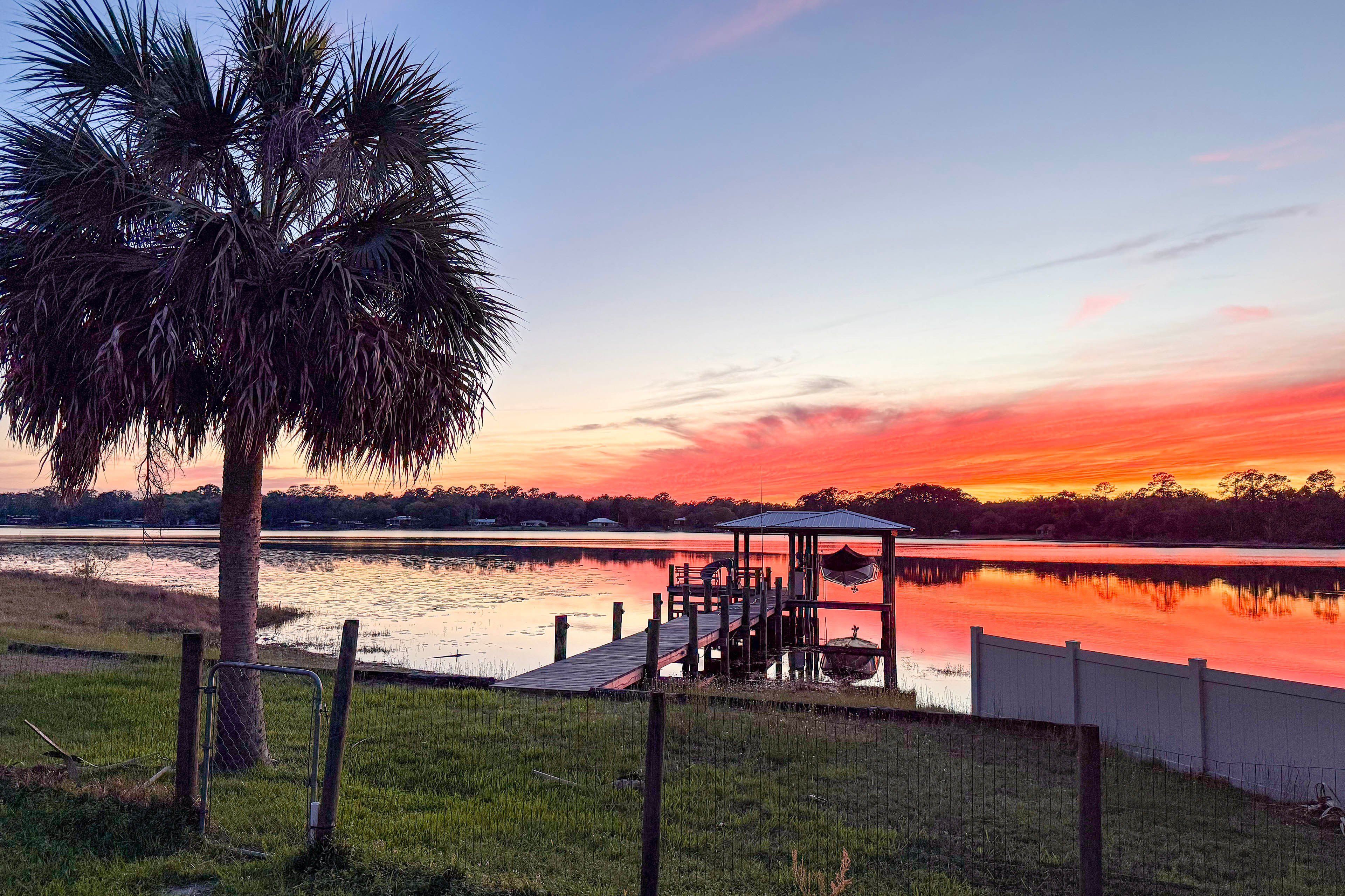 A wooden dock extending into a calm body of water with a sunset in the background.