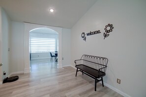 A spacious room with a dark wooden bench, a wall-mounted welcome sign, and a view into another room through an arched doorway. - The Boise Retreat | Spacious Home, Game Room! (Boise)