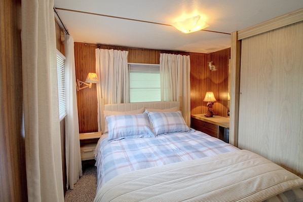A bedroom with a bed, curtains, a nightstand, a lamp, and a window with blinds. - Harlan County Lake View Cabin by ATV Trails (Republican City)