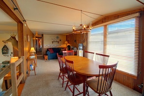 A dining area with a wooden table and chairs, a chandelier, and a view through large windows. - Harlan County Lake View Cabin by ATV Trails (Republican City)