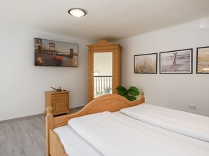 A bedroom with a wooden bed, a nightstand, a mirror, and wall-mounted artwork. - Lütt Stuuv, Germany (Sylt)