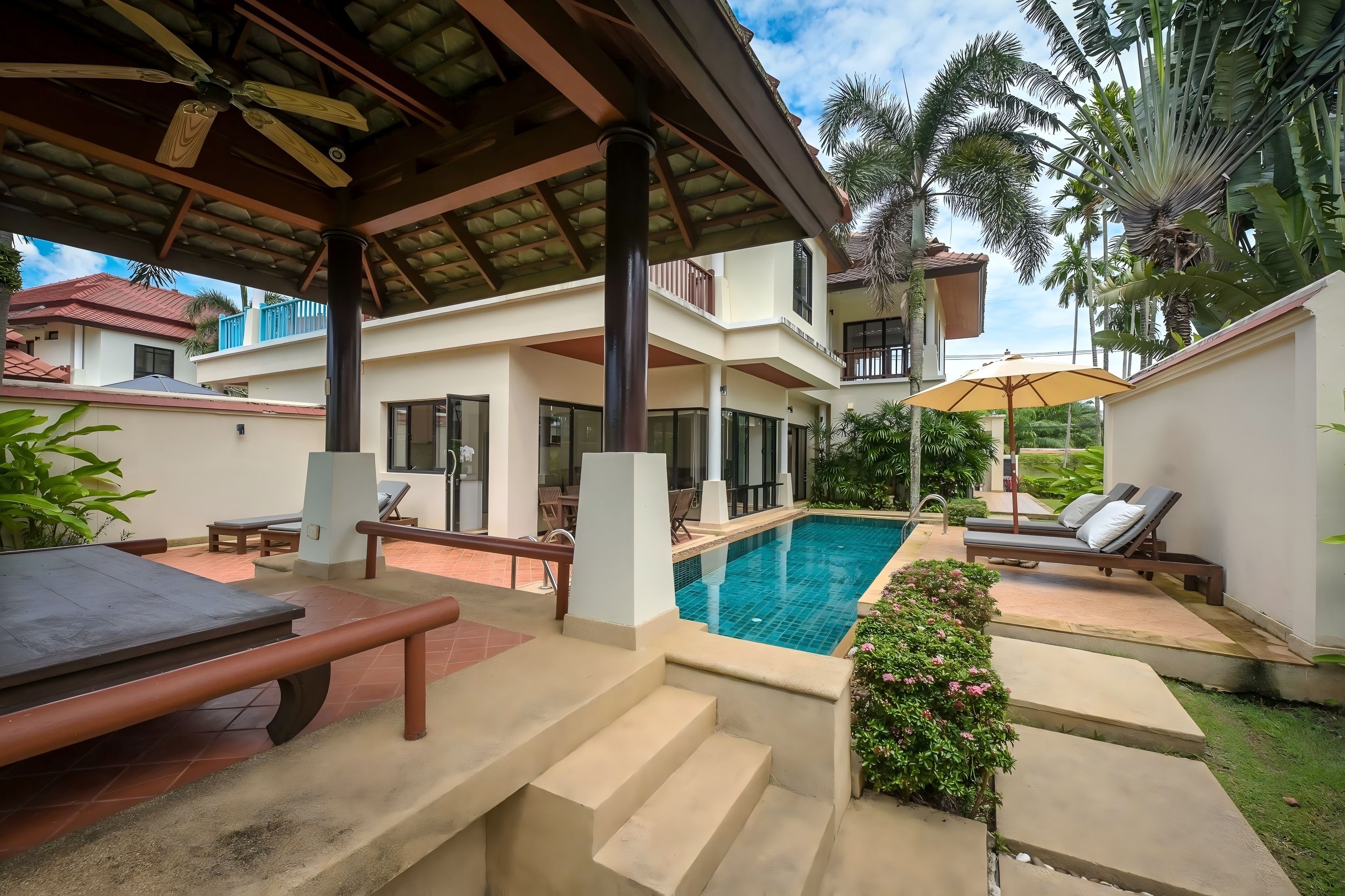 A poolside area with lounge chairs, a covered seating area, and a staircase leading to a second level.