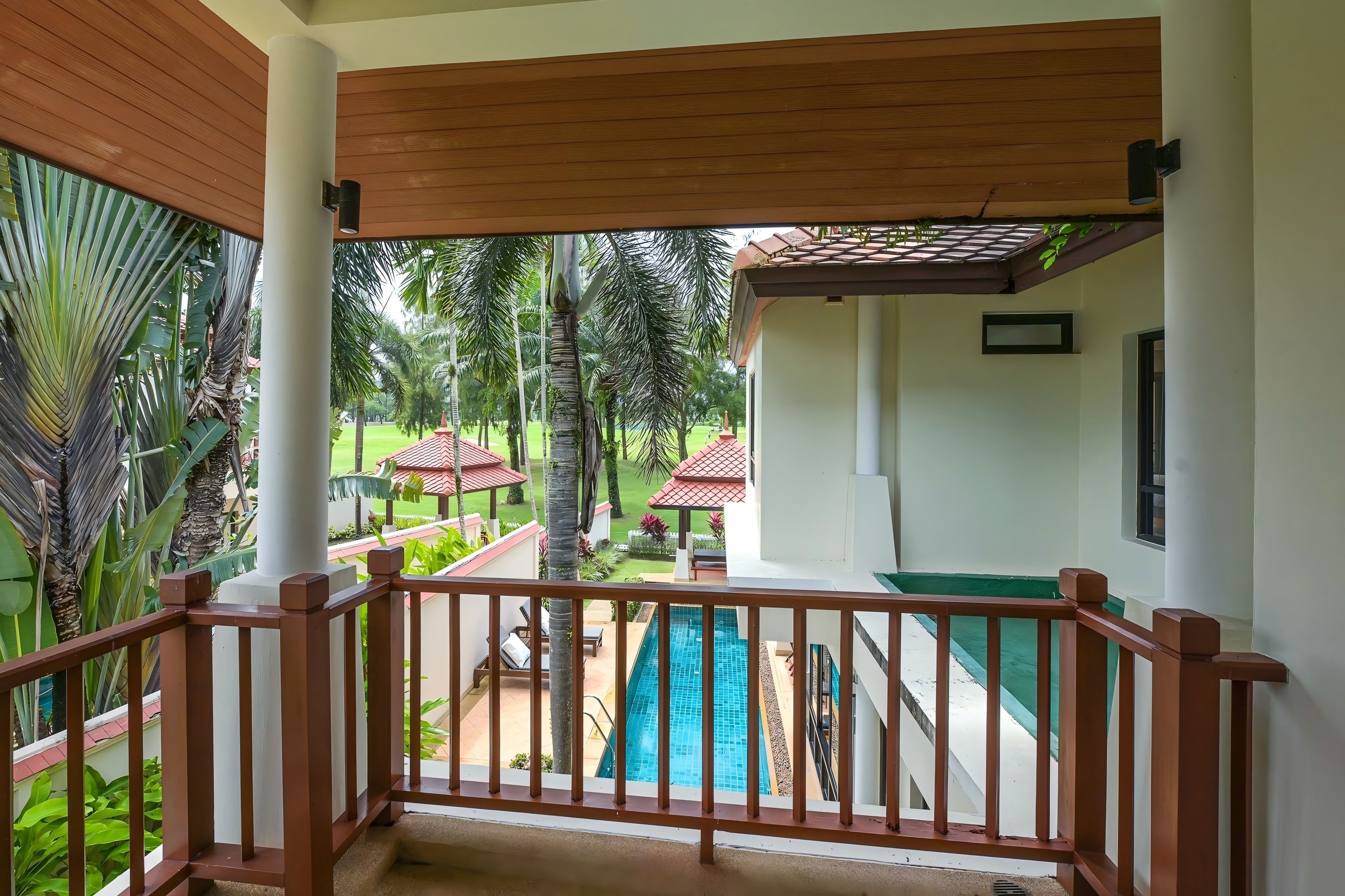 A covered balcony with a view of a swimming pool and a garden.