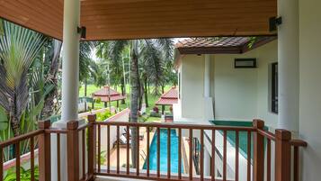 A covered balcony with a view of a swimming pool and a garden.