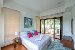 A hotel room with a bed, a painting, a balcony with a view of palm trees, and a wooden floor. - Laguna 4bedroom Luxury Villa  (Thalang District)