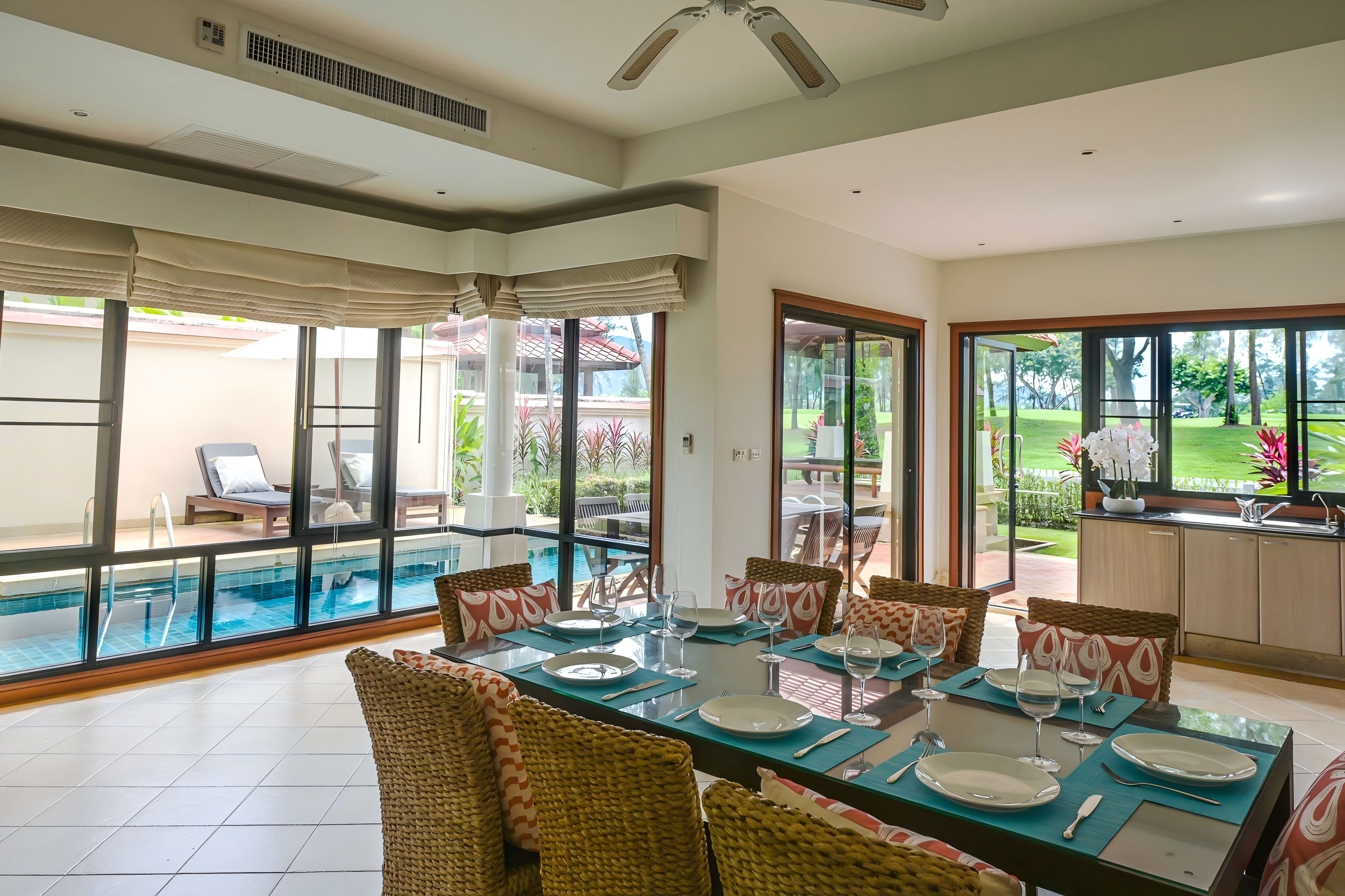 A spacious indoor area with a dining table set for six, large windows, and a view of an outdoor swimming pool.