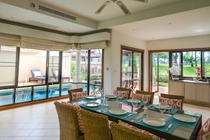 A spacious indoor area with a dining table set for six, large windows, and a view of an outdoor swimming pool. - Laguna 4bedroom Luxury Villa  (Thalang District)