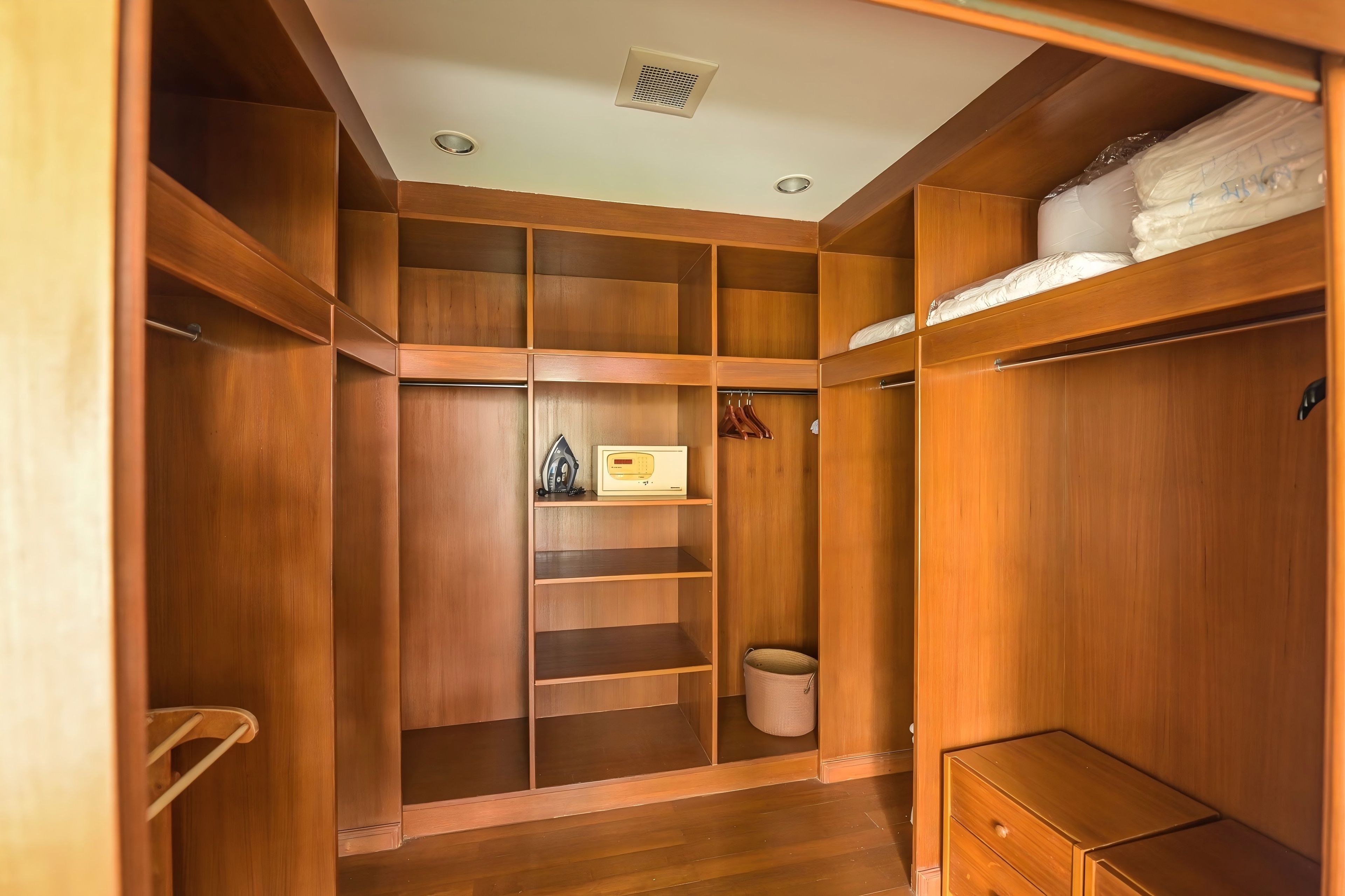 A walk-in closet with multiple shelves, hanging space, and a small wooden cabinet.