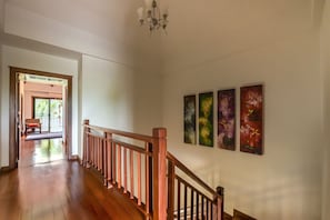 A hallway with wooden flooring, a wooden railing, and three abstract paintings on the wall.