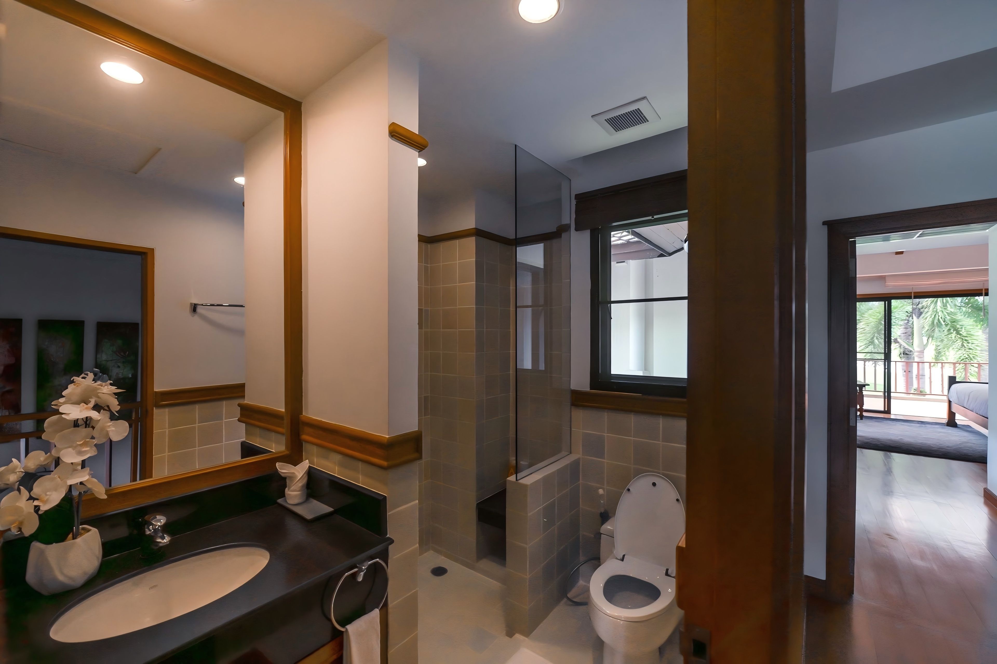 A modern bathroom with a large mirror, a sink, a toilet, and a shower area.